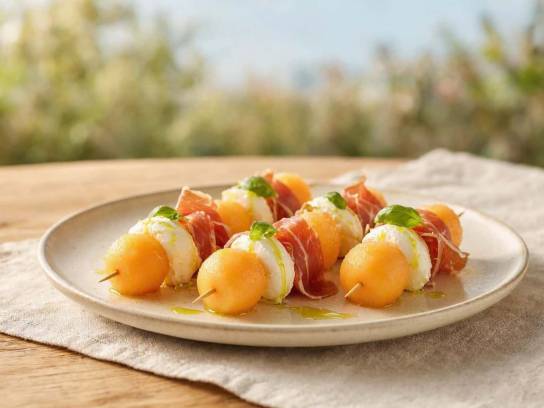 Brochettes de melon charentais au jambon de pays et chèvre frais au basilic dans une assiette