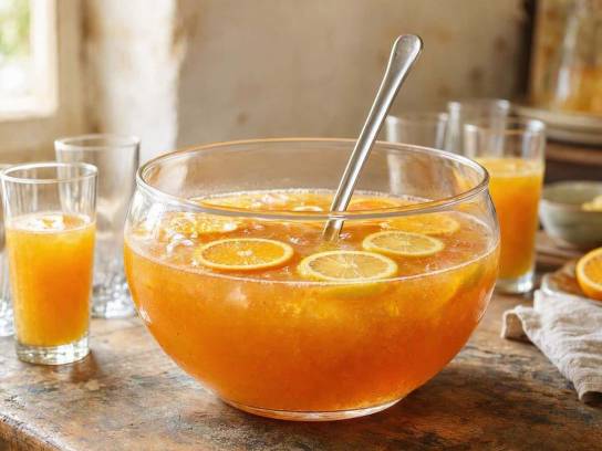 Punch charentais traditionnel avec rondelles d’orange et citron dans un grand saladier, posé sur une table en bois.