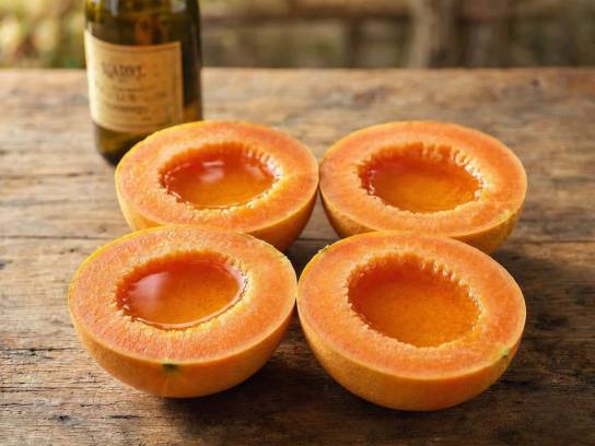 Demi-melons de Charente au Pineau des Charentes vieux. Entrée d'été traditionnelle charentaise avec fruits mûrs et alcool ambré sur table en bois.