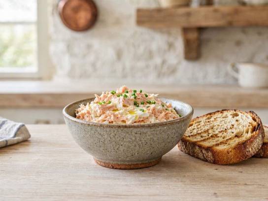 Rillettes de truite maison au fromage frais dans un bol en céramique avec pain de campagne et ciboulette.