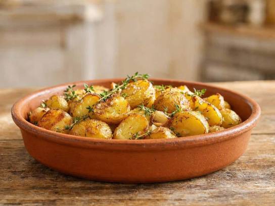 Pommes de terre grenaille rôties au thym et à l'ail, servies dans un plat en terre cuite rustique.