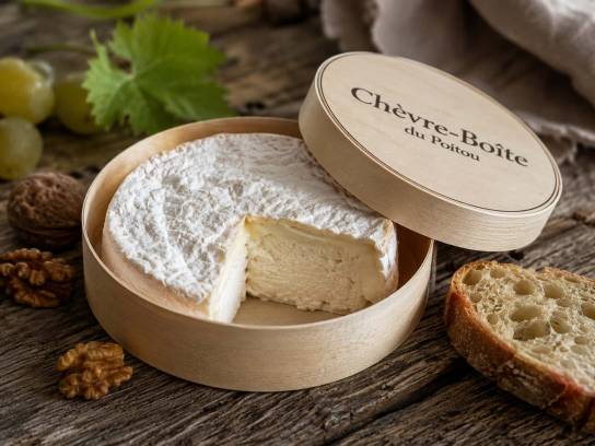 Fromage Chèvre-Boîte artisanal entamé sur une table en bois, révélant sa pâte crémeuse dans sa boîte en bois d'épicéa.