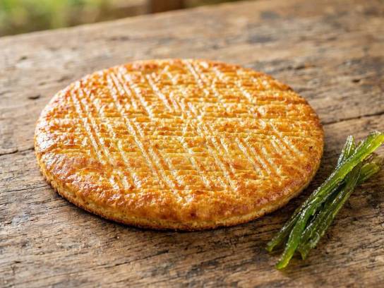 Galette charentaise traditionnelle ronde et plate gravée de motifs en losanges, posée sur une table en bois rustique avec une branche d'angélique confite.